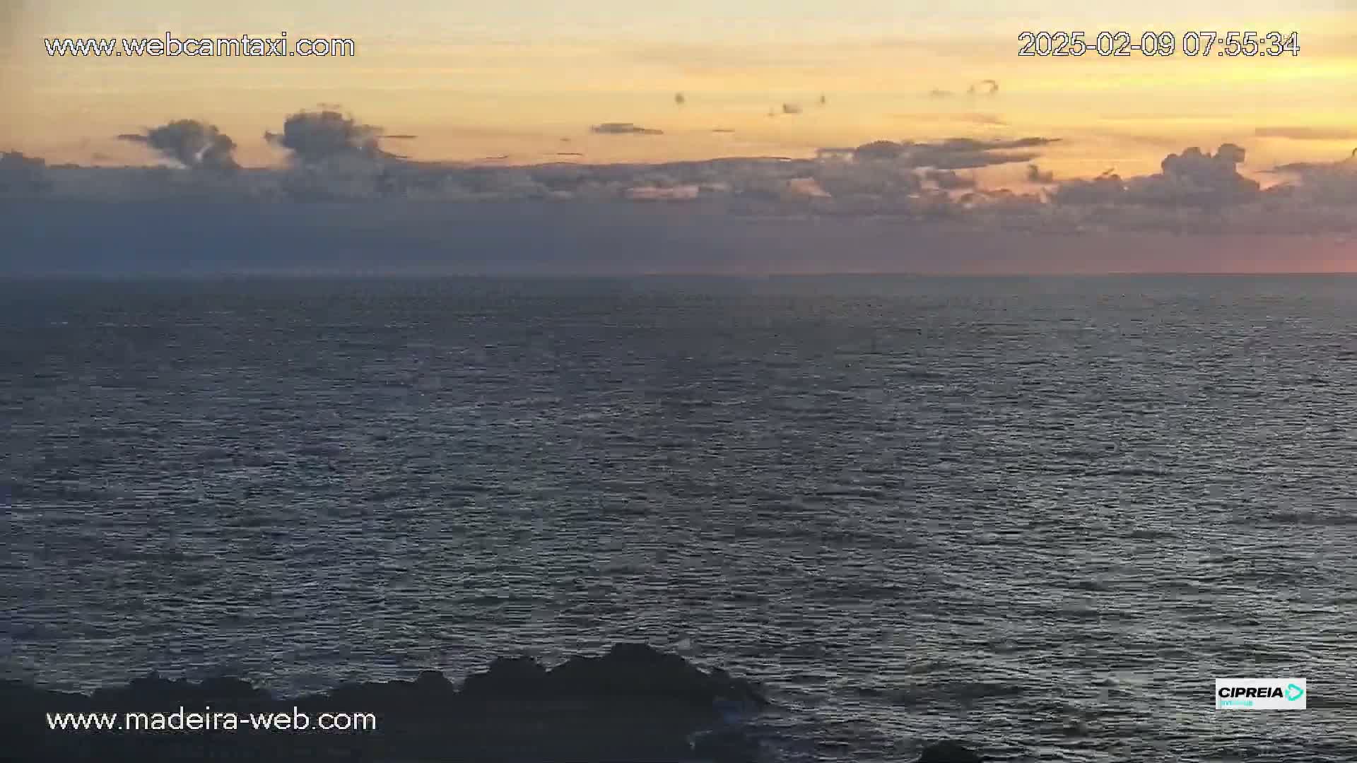 A calm ocean at sunset with a mostly cloudy sky.