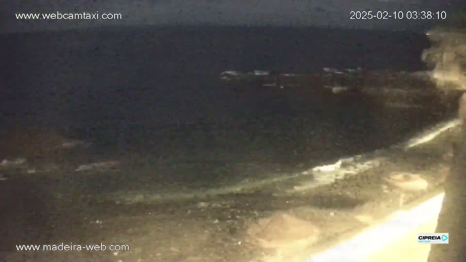 A dark, nighttime view of a rocky shoreline with small waves lapping at the rocks and dark ocean extending into the distance.