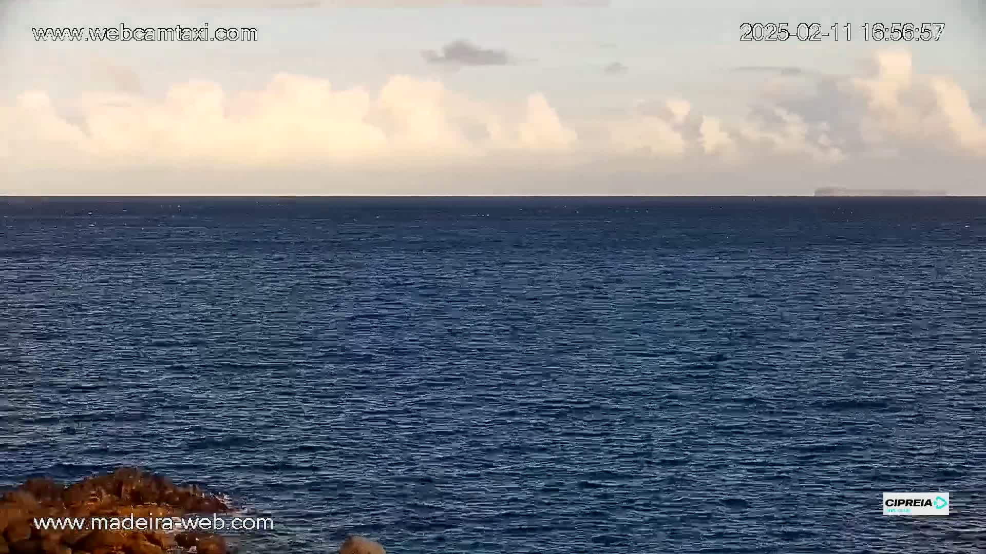A mostly clear sky with some clouds sits above a dark blue ocean meeting a distant landmass.