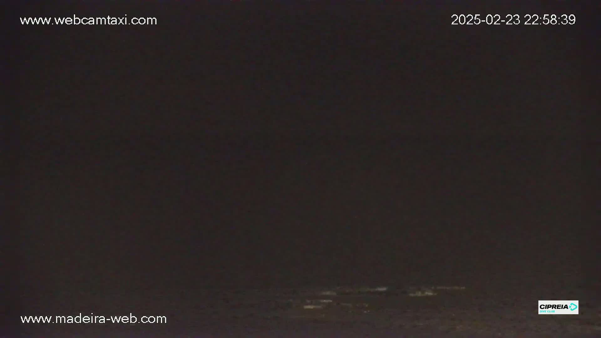 A dark, nighttime view of a mostly calm body of water under a nearly cloudless sky.
