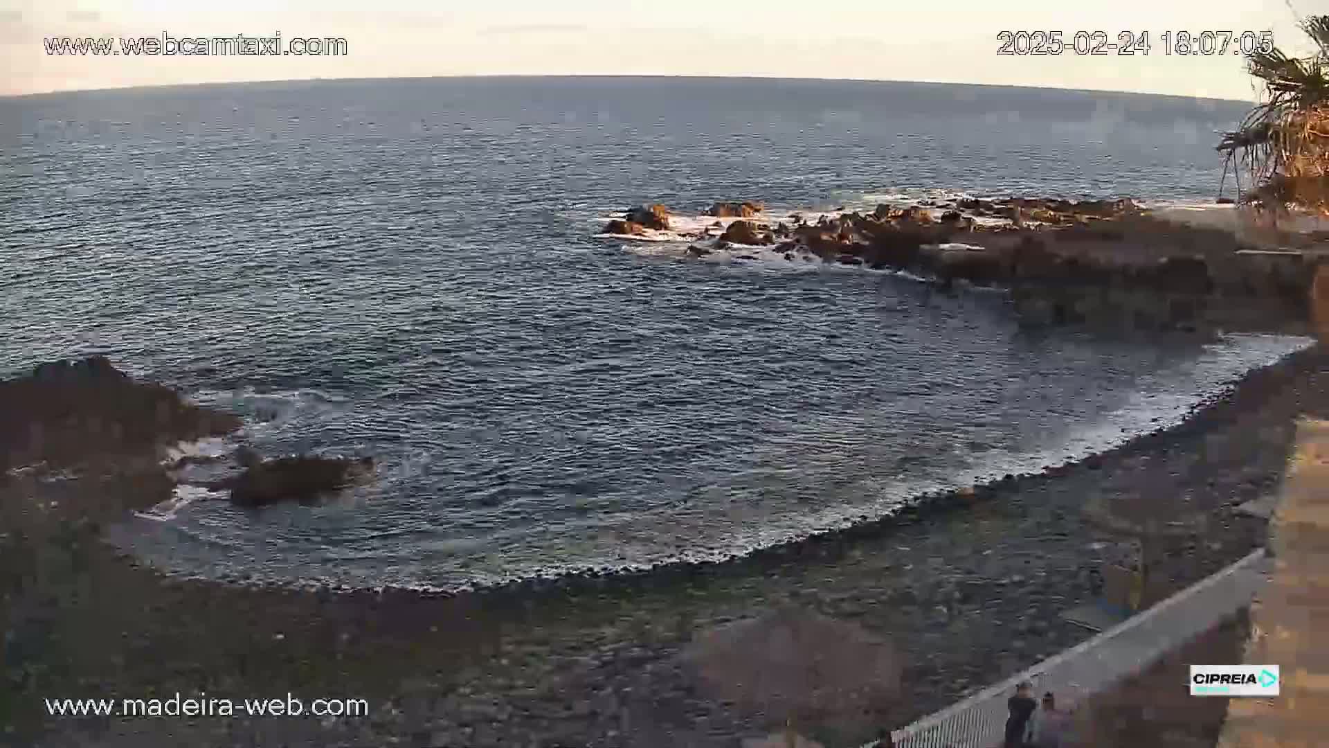 A rocky shoreline curves around a calm, dark-blue ocean under a twilight sky.