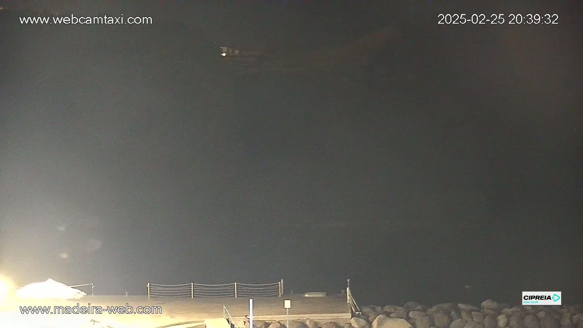 A nighttime view of dark water, a dark shoreline with rocks, and a small section of a pier.