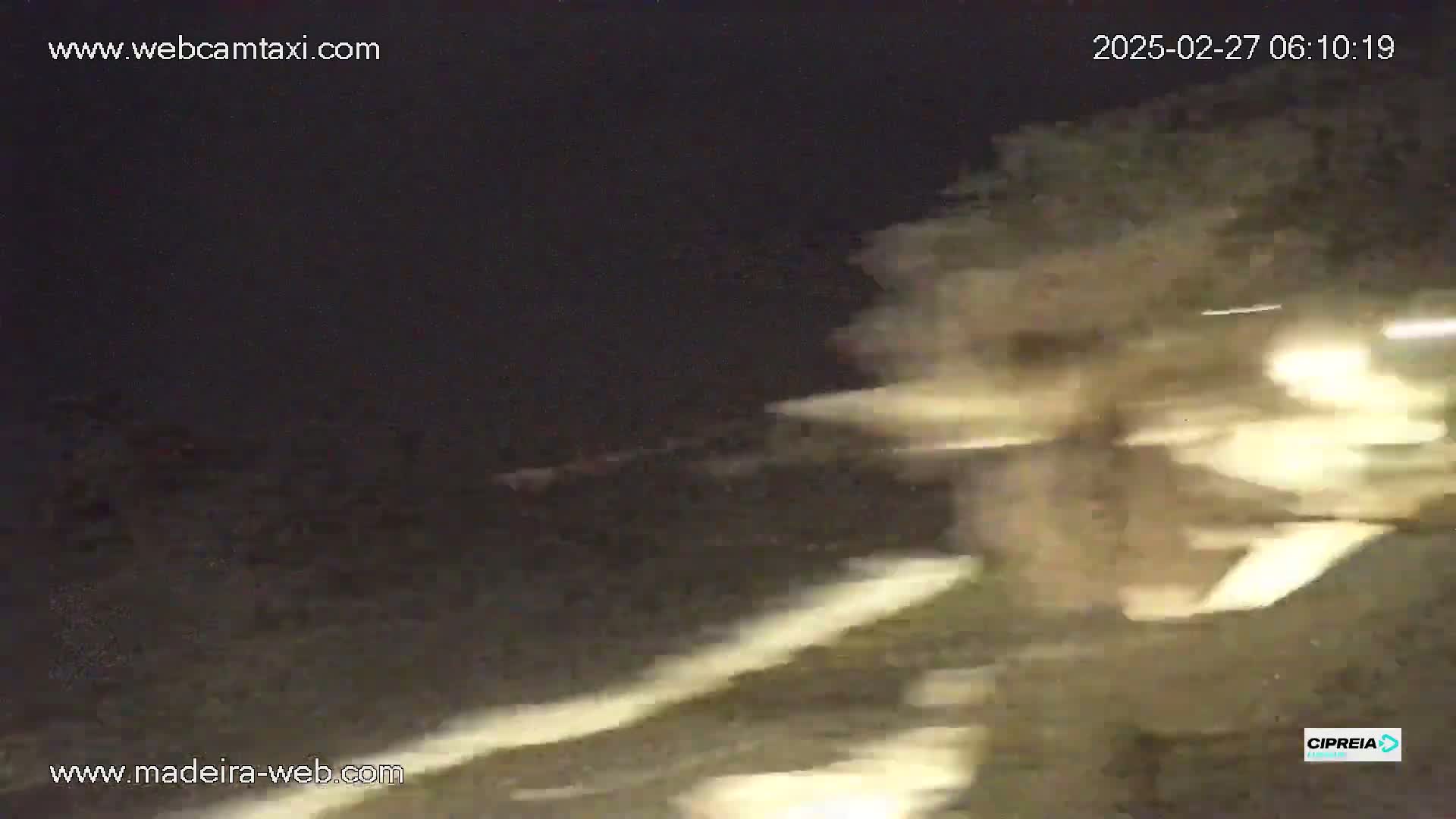 A blurry nighttime image shows a dark, possibly stormy, scene with bright lights in the distance.
