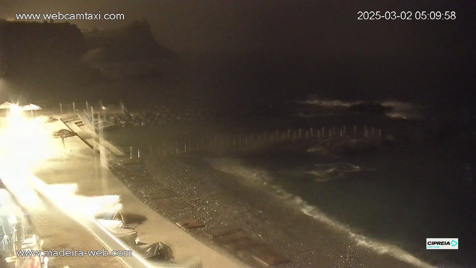 A nighttime, rainy view of a pebble beach with dark, choppy ocean waves rolling ashore.