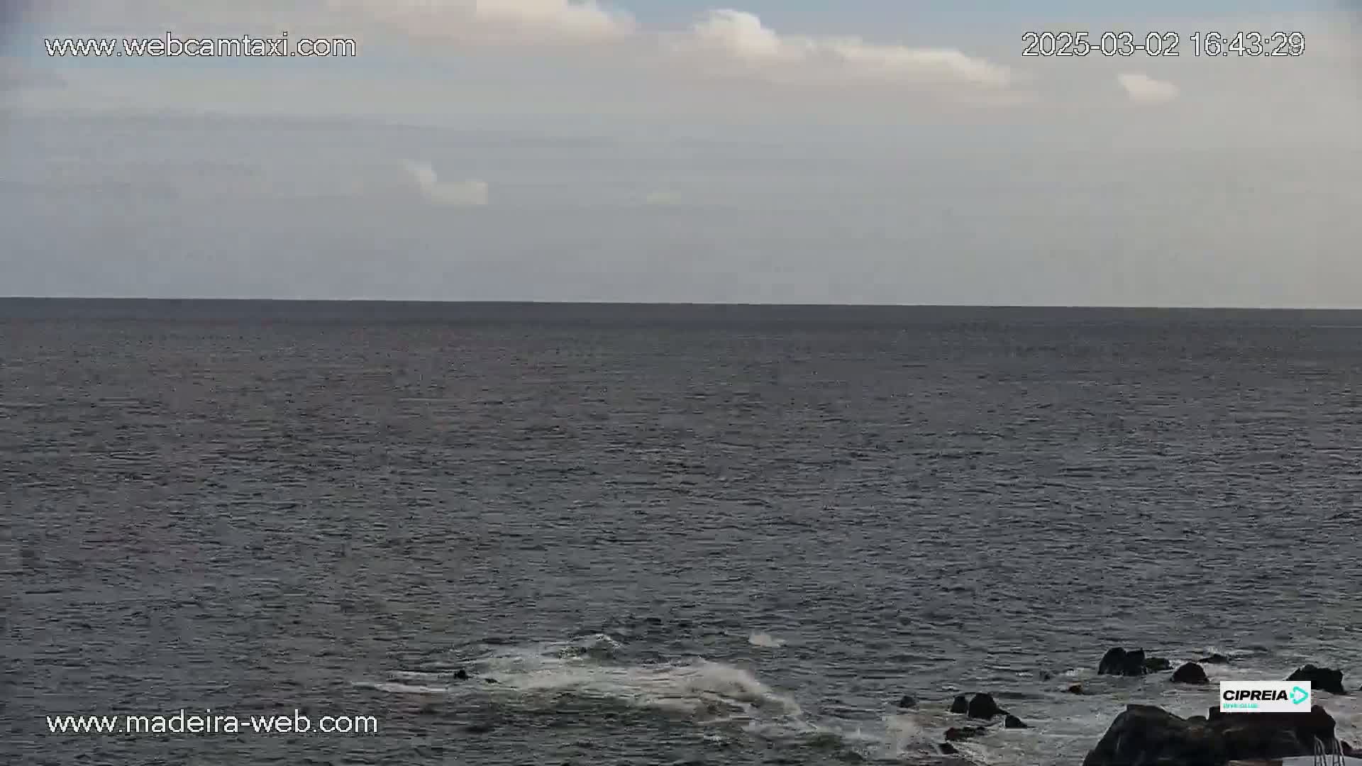 A mostly cloudy day shows a dark ocean meeting a rocky shoreline with some small waves.