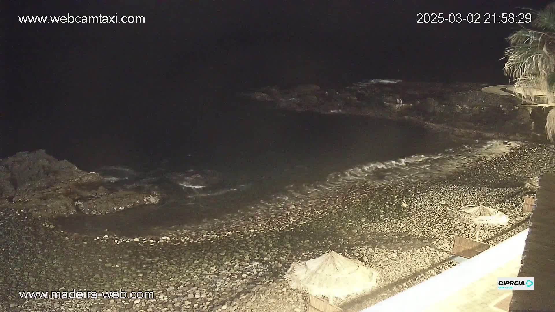 A dark, rocky beach at night with gentle waves lapping the shore, under a clear, starless sky.