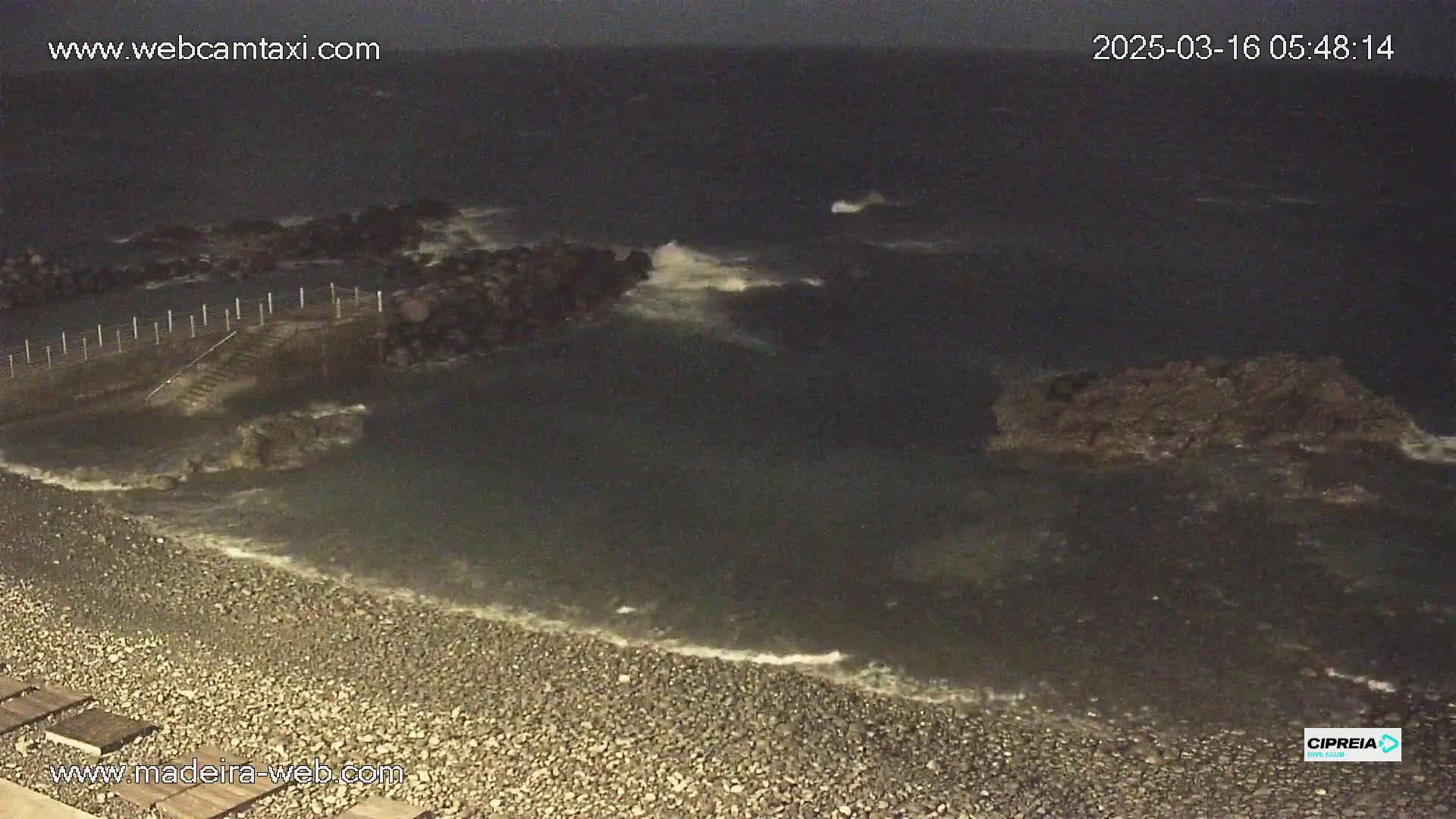 A dark, rocky shoreline meets a choppy sea at night under overcast skies.