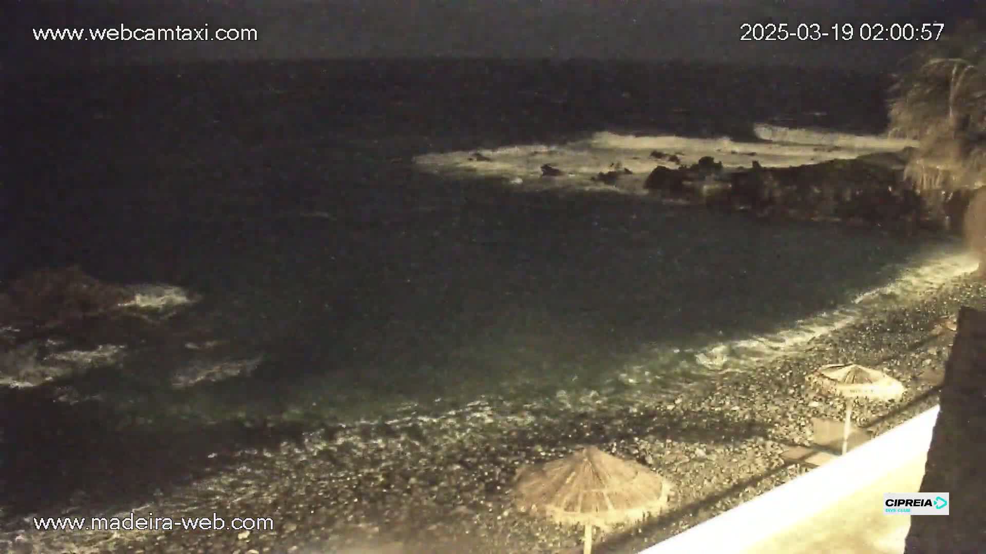 A dark, rocky shoreline is lapped by restless waves under a nighttime sky.