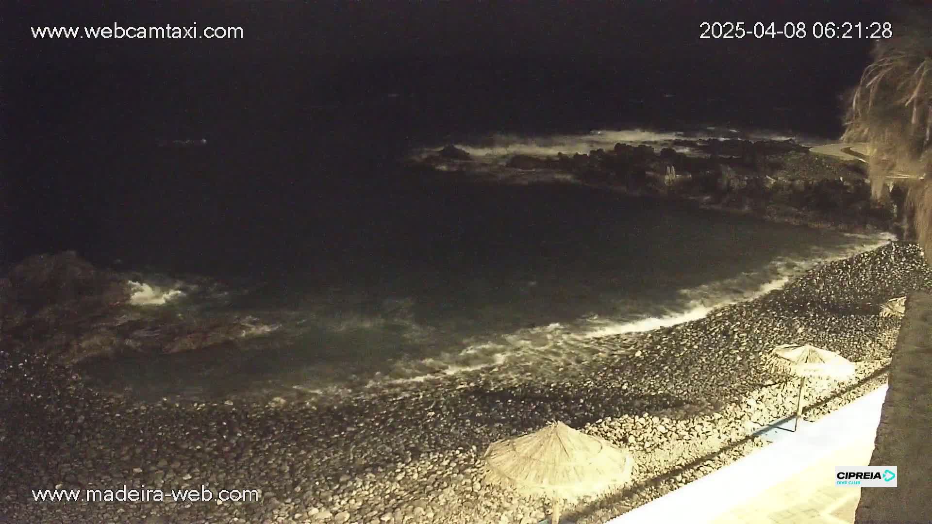 A rocky beach at night with waves gently lapping the shore under a dark sky.