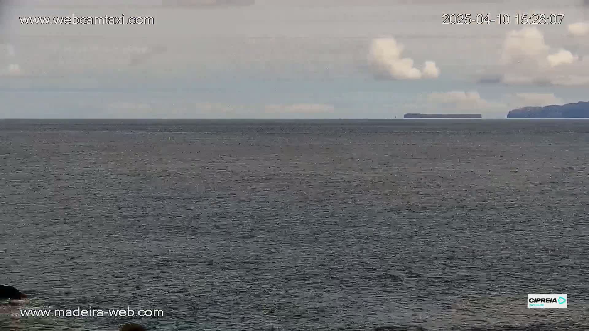 A calm, gray ocean stretches to the horizon under a partly cloudy sky, with dark landmasses visible in the far distance.
