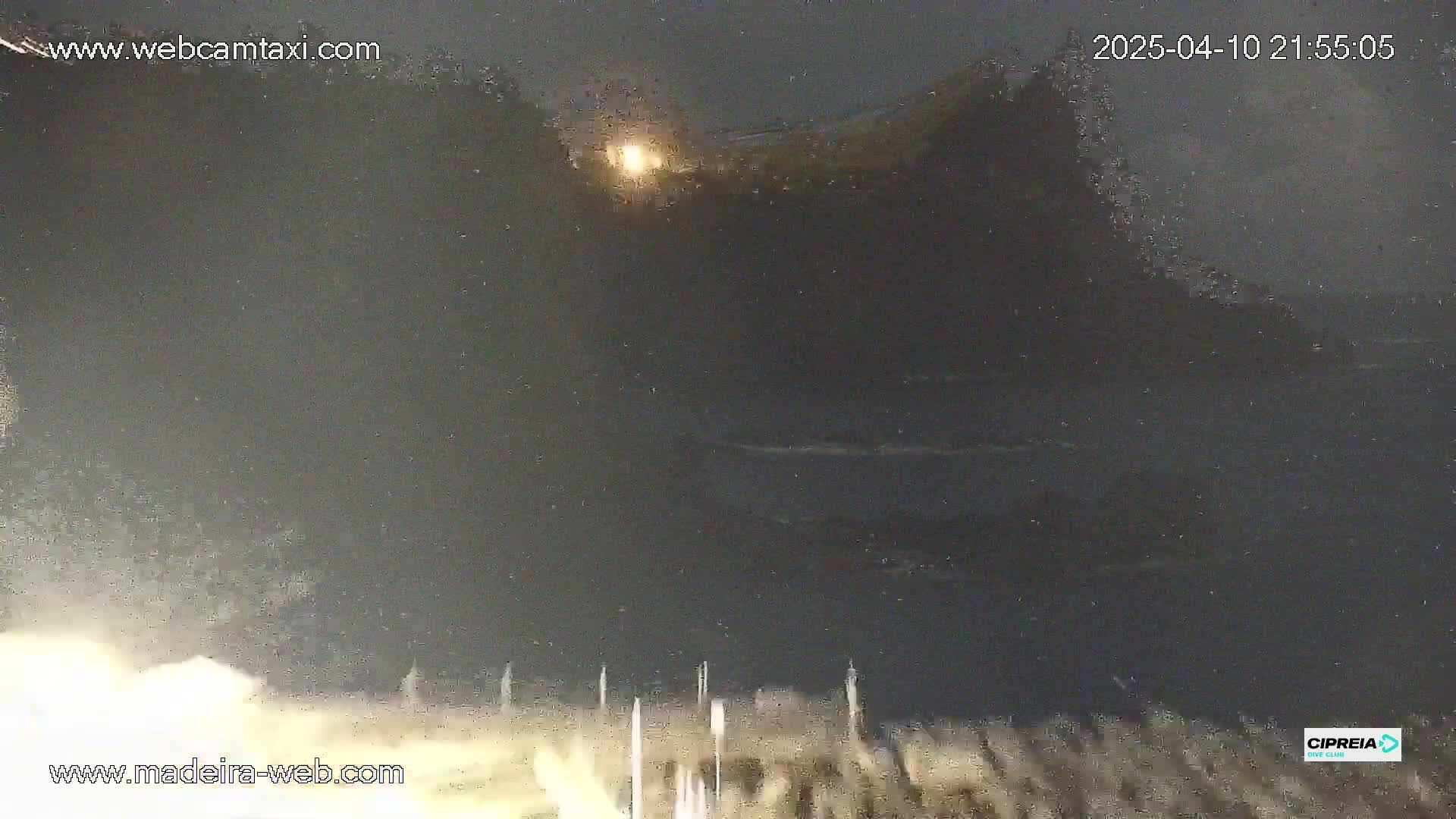 A nighttime, blurry view of a dark body of water with a distant, indistinct shoreline and a bright light visible through a hazy atmosphere.
