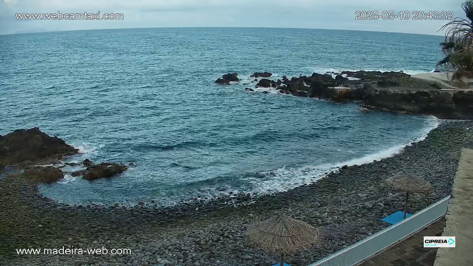A rocky, pebble beach meets a dark-blue ocean with small waves under an overcast sky.