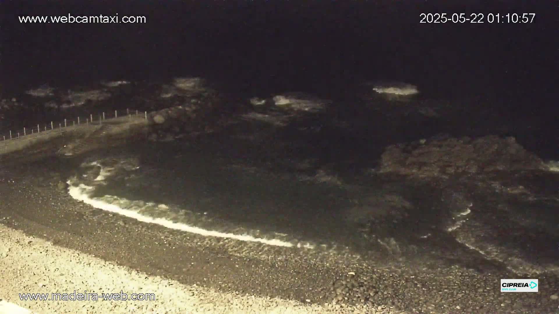 Dark, nighttime waves lap a pebble shore under a clear, moonless sky.