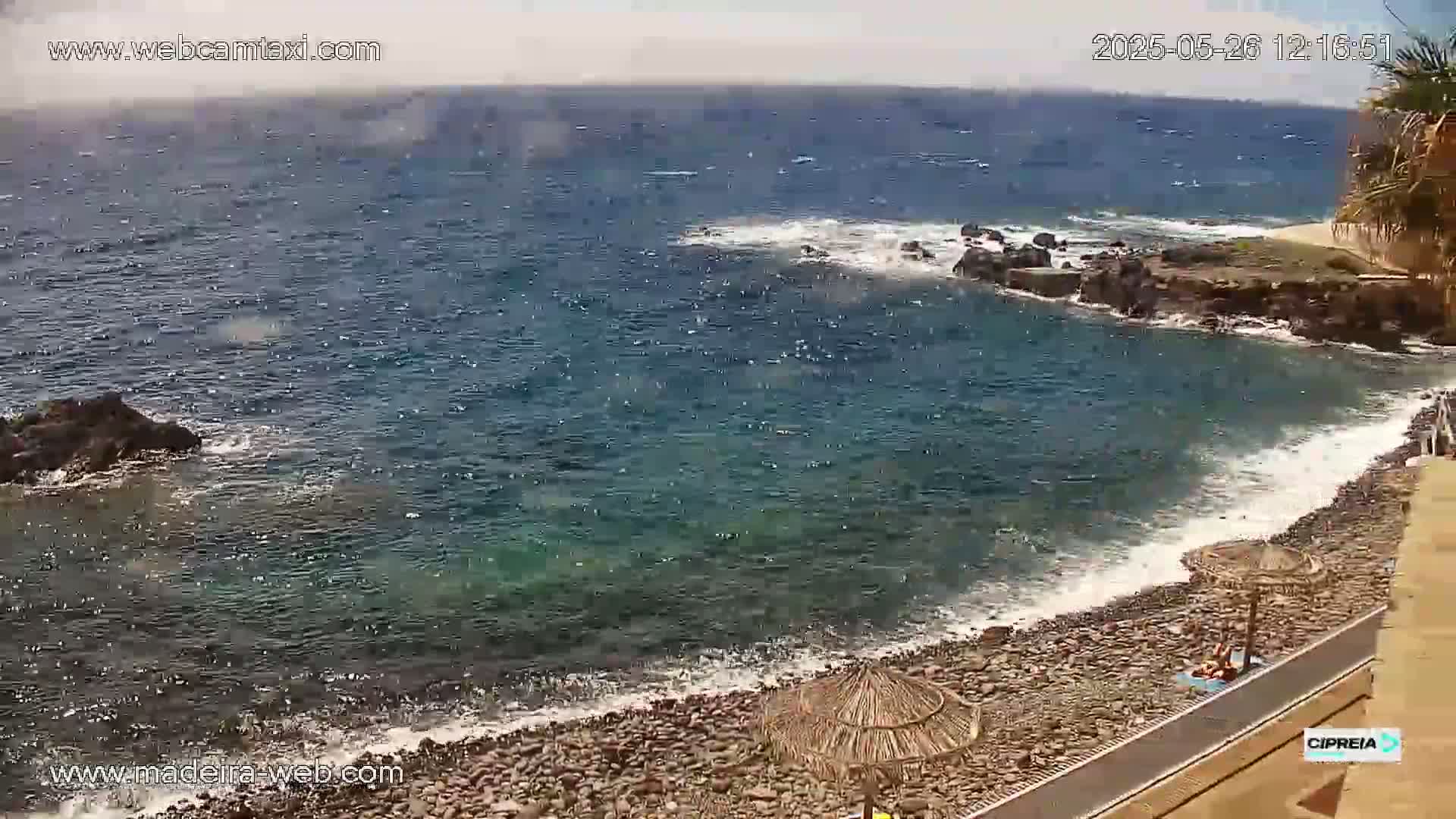 A rocky beach with small waves lapping the shore on a partly cloudy day.