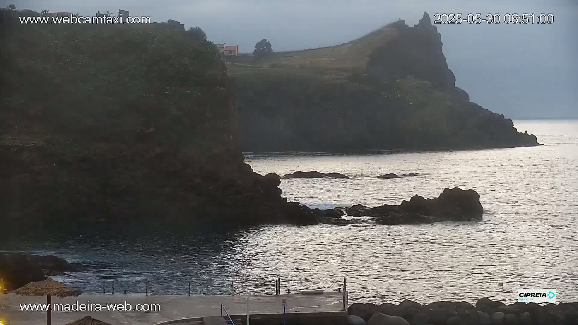 Dark, rocky cliffs overlook a calm, gray ocean under an overcast sky.