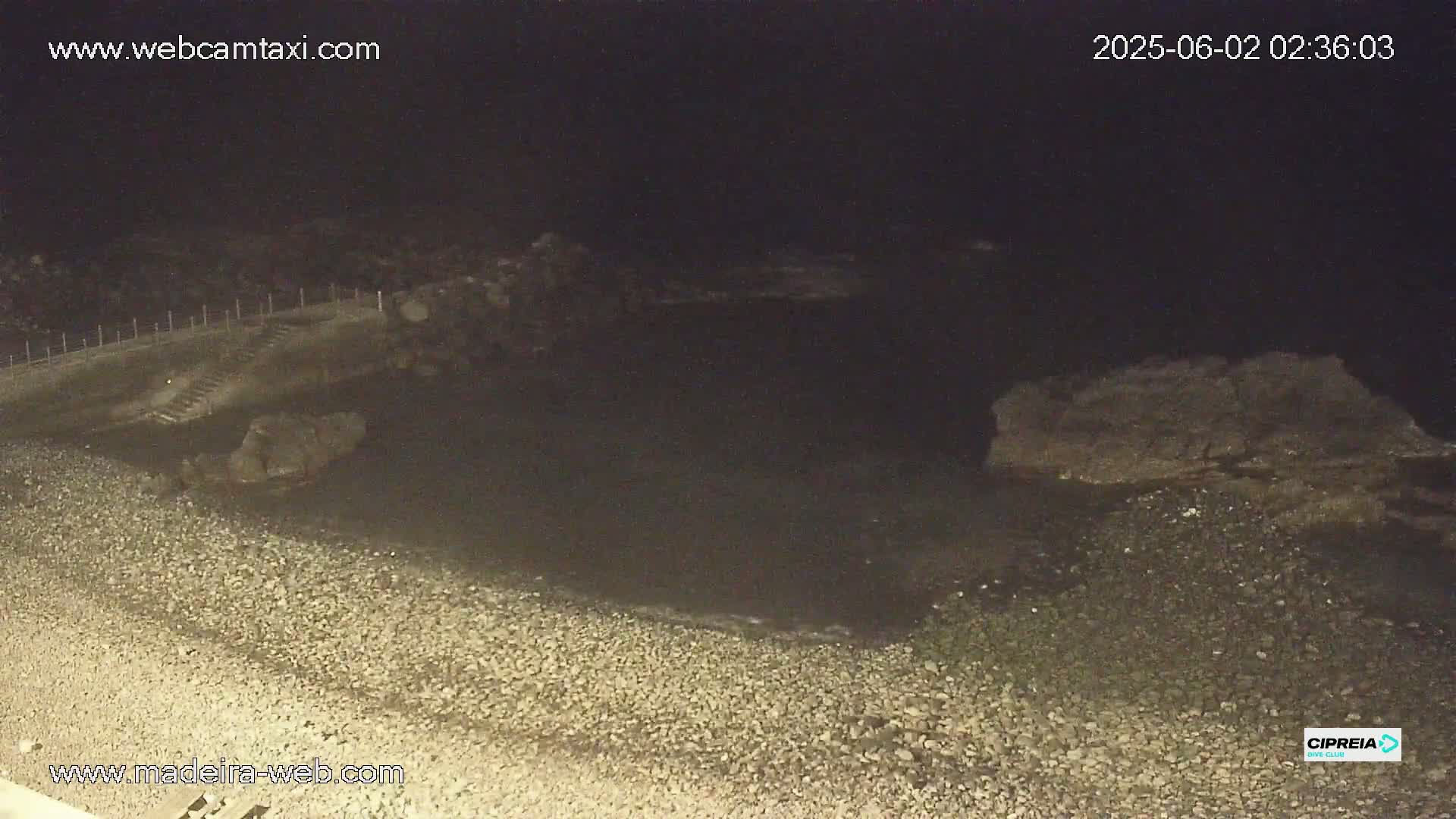 A dark, rocky shoreline meets a calm, dark body of water at night.