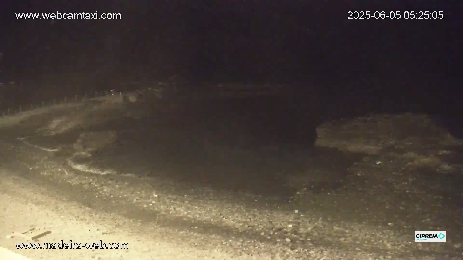 A dark, rocky shoreline is visible at night, with some small waves lapping at the shore under a clear, dark sky.