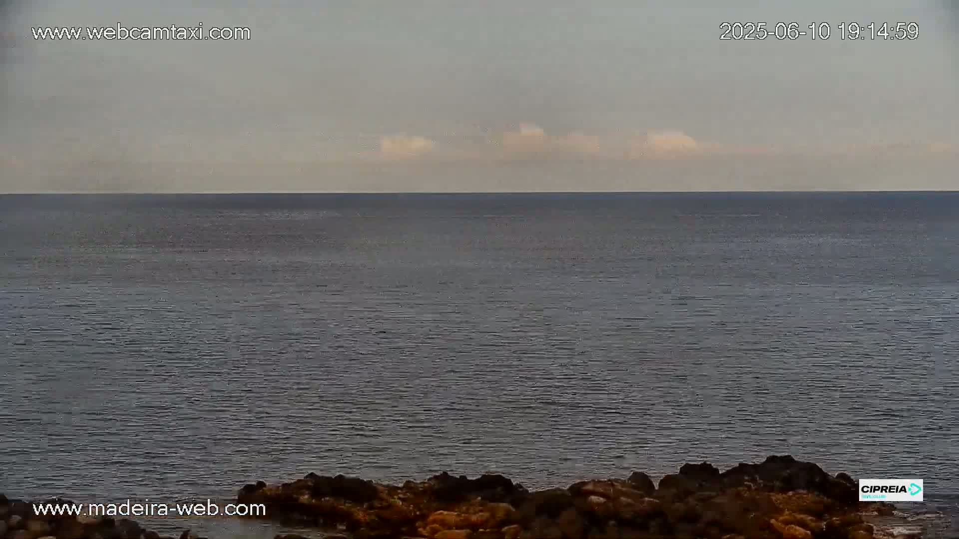 A calm, dark-grey ocean stretches to a horizon under a mostly cloudy, light-grey sky.