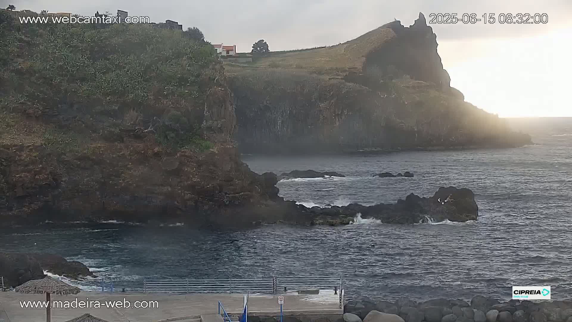 A rocky coastline with a small building on a cliff overlooking dark, slightly choppy ocean water under an overcast sky.