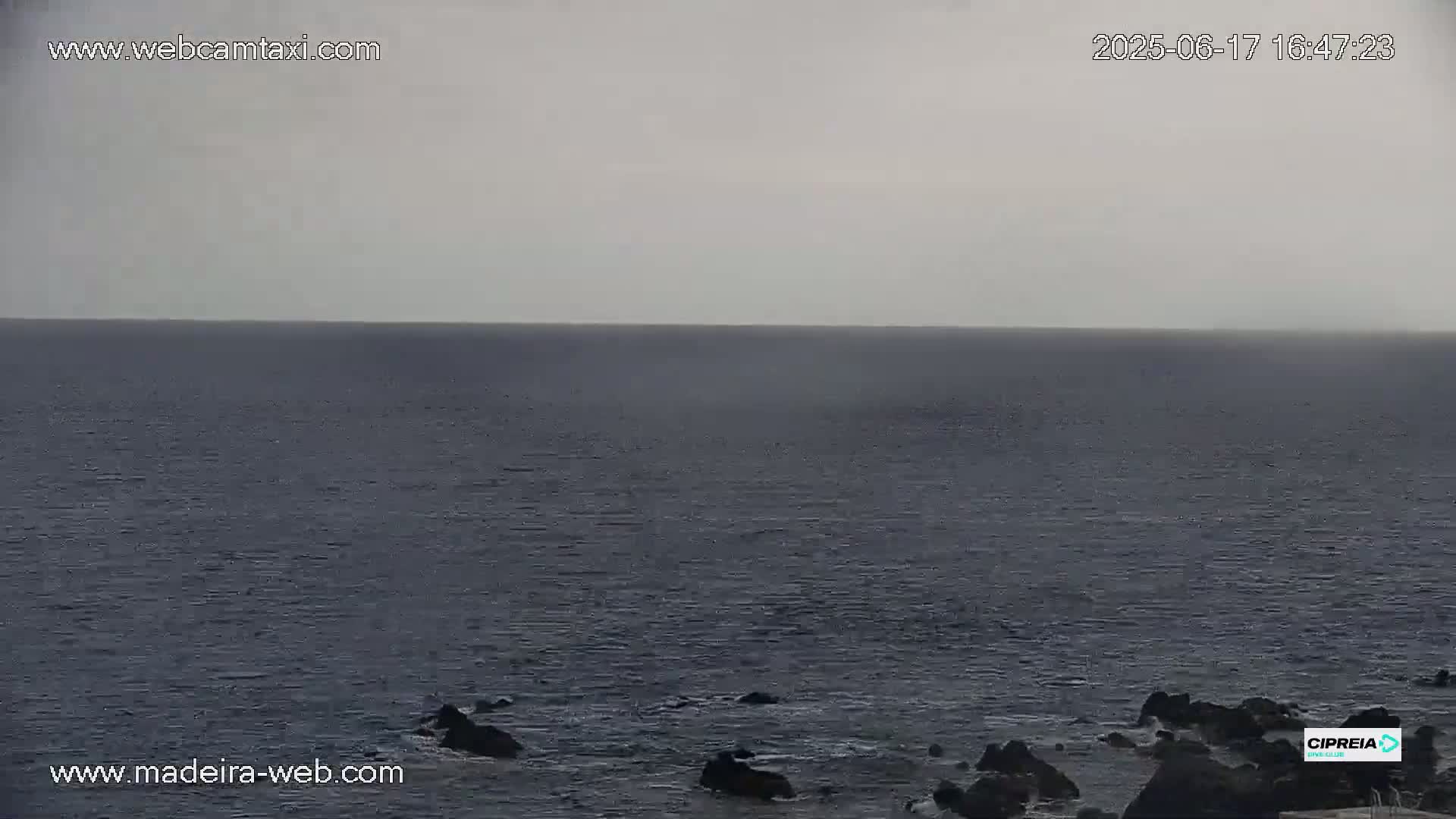 A dark, overcast sky hangs over a calm, dark-blue ocean meeting a rocky shoreline.