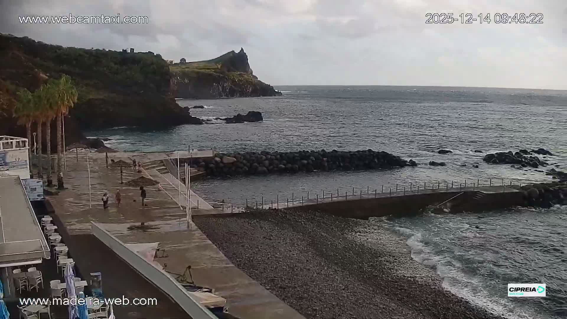 A blurry, dark outdoor scene at night shows a railing or structure in the foreground, with countless illuminated specks filling the air, indicative of heavy rain or mist.