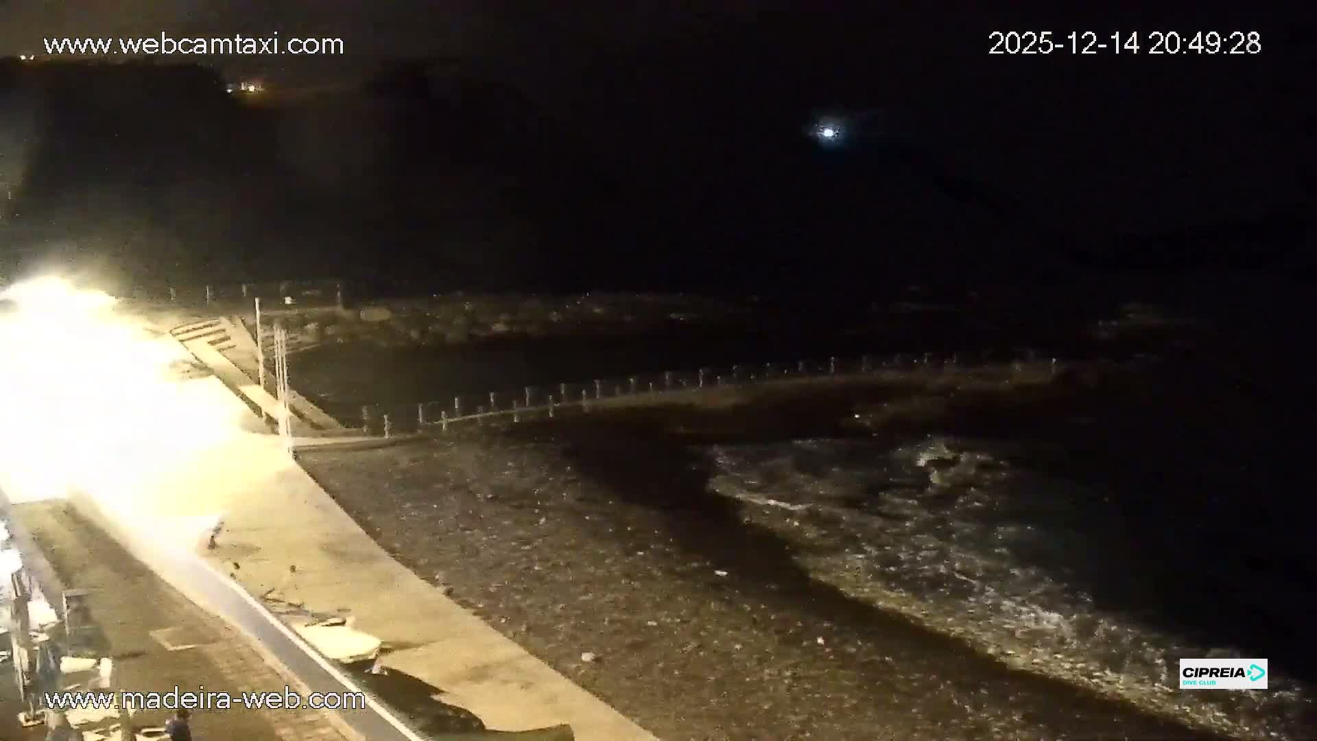 A blurry, dark outdoor scene at night shows a railing or structure in the foreground, with countless illuminated specks filling the air, indicative of heavy rain or mist.