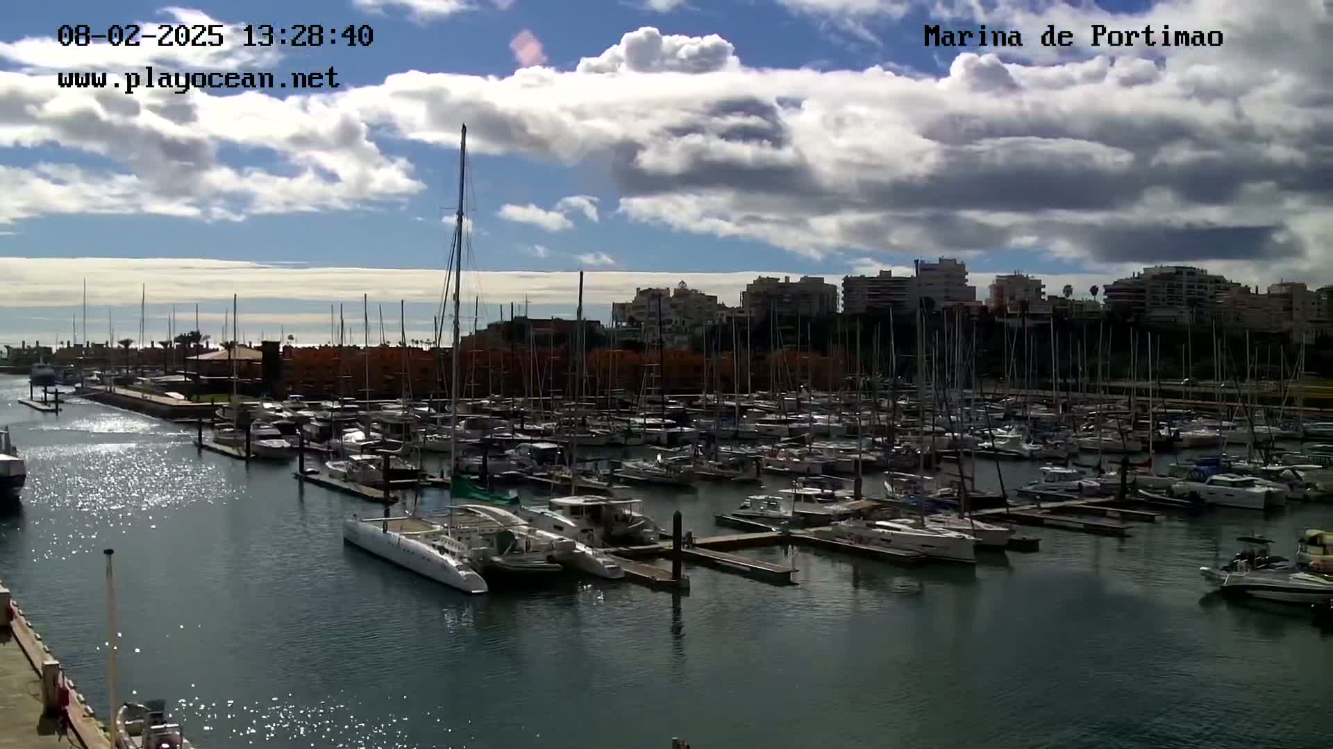 A marina filled with numerous sailboats and motorboats under a partly cloudy sky.