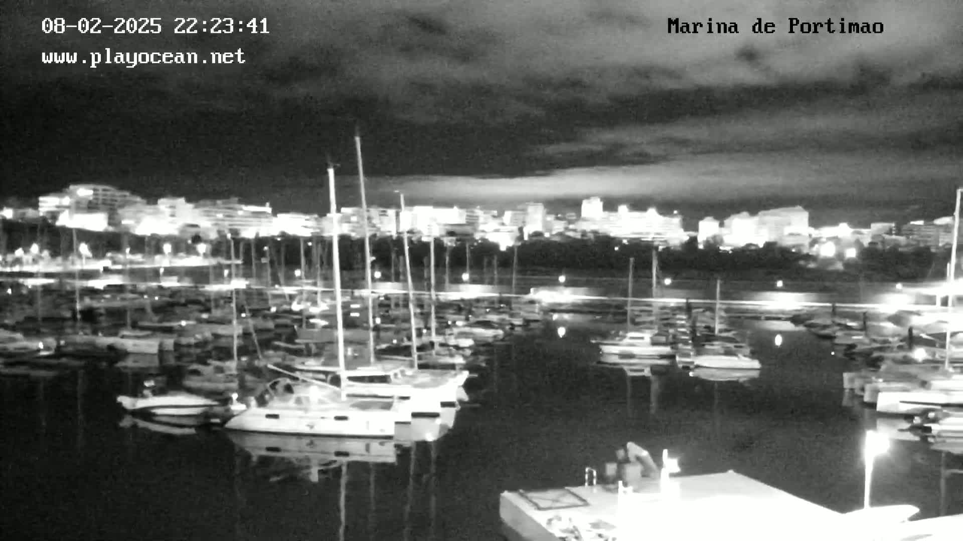 A nighttime view of a marina filled with sailboats and motorboats under a cloudy sky.