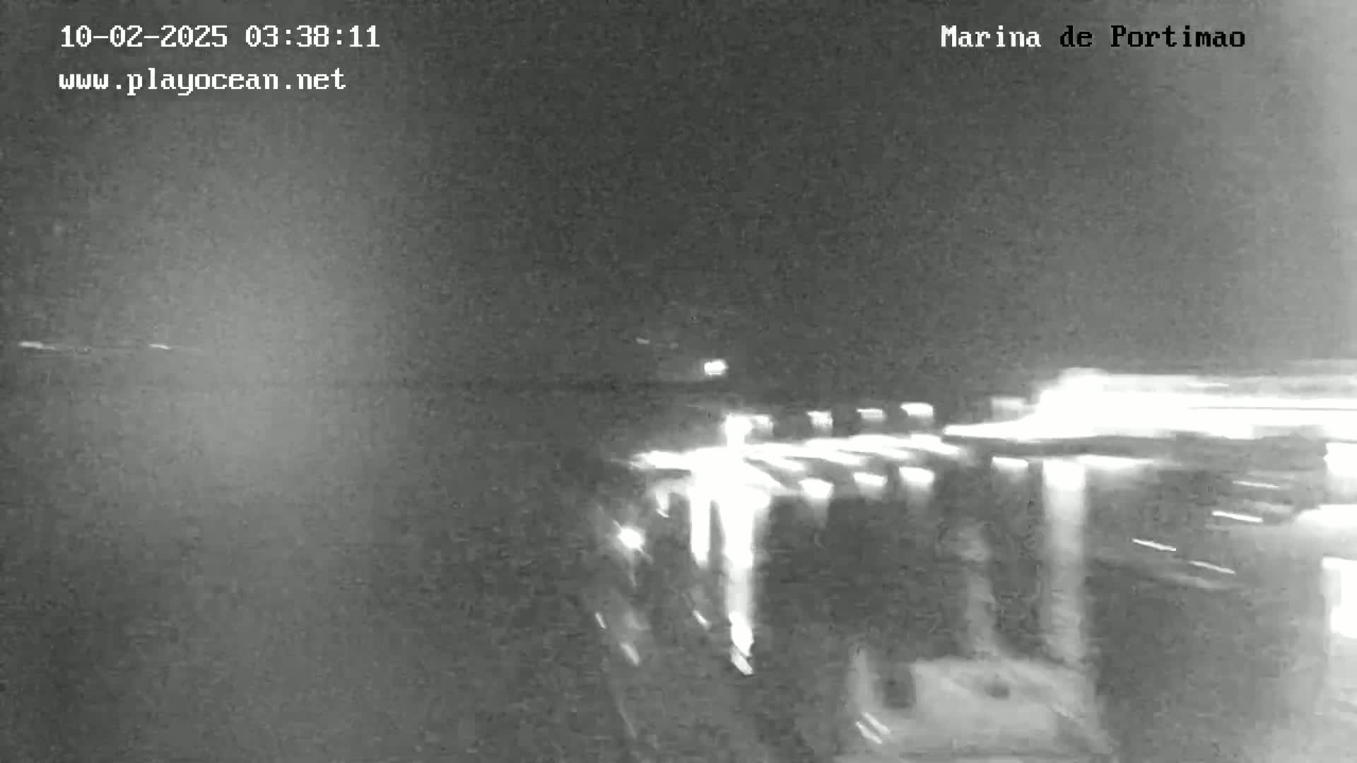 A nighttime, low-light view of a marina with blurry lights from boats and possibly vehicles in the foreground.