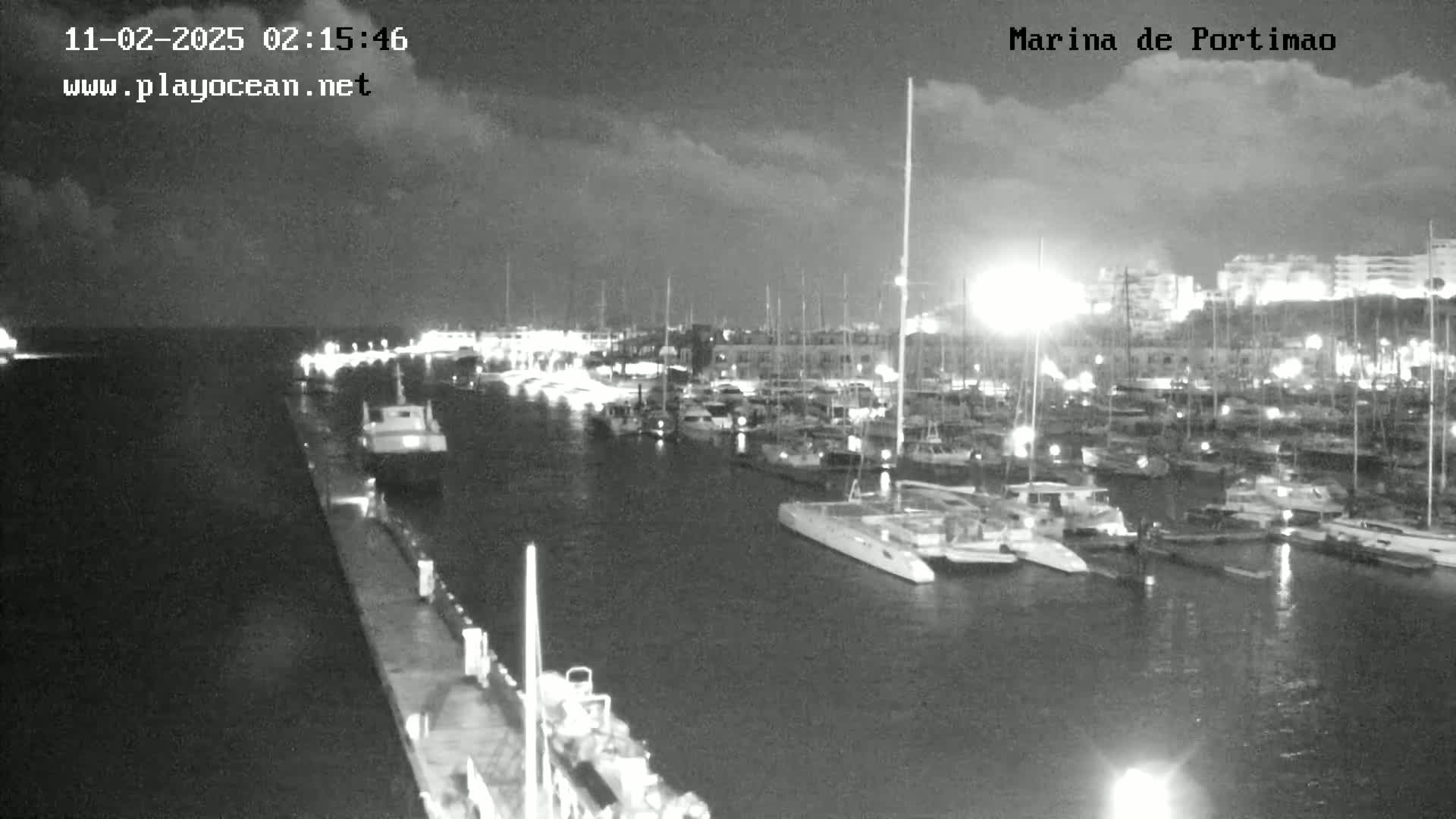 A nighttime, overcast view of a marina filled with many boats and yachts, some of which are lit.