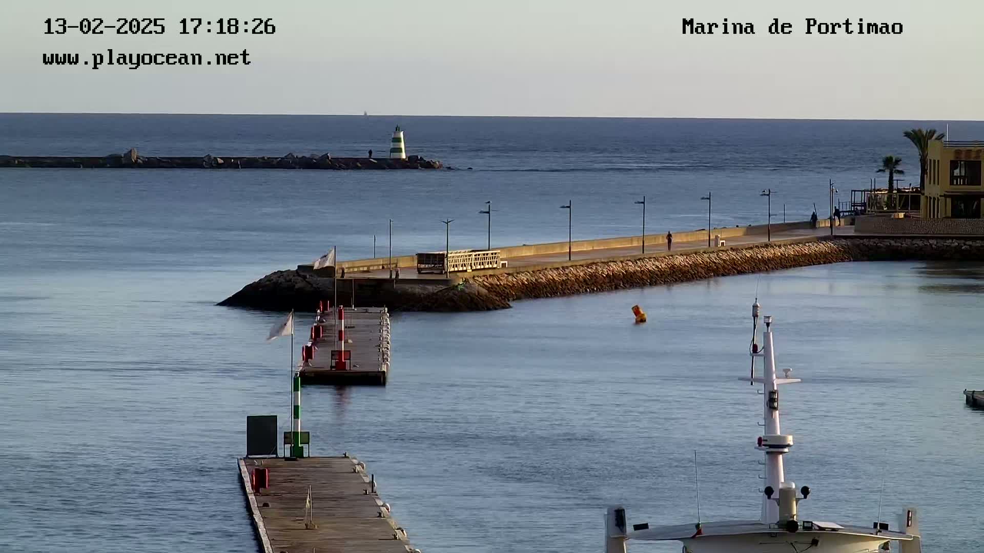 A calm harbor scene with a long pier extending into the water under a clear, daytime sky.