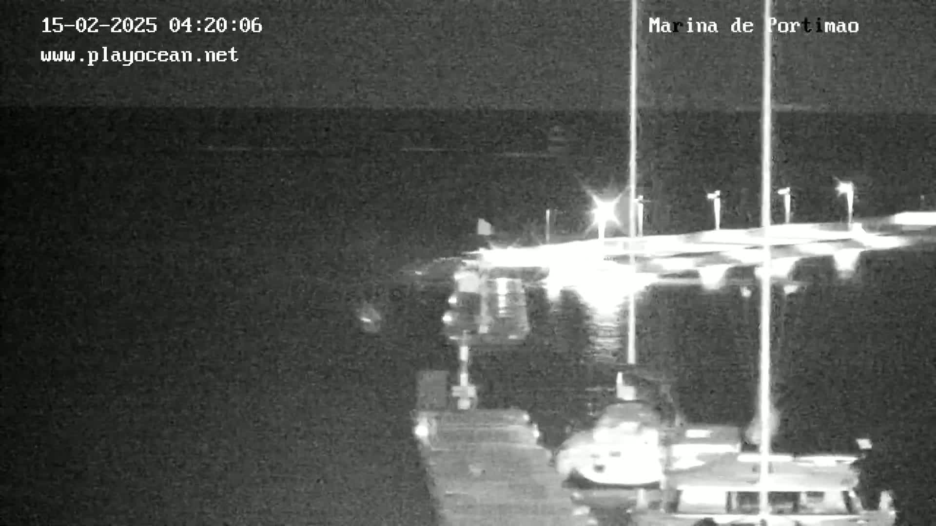 A nighttime, low-light image shows a marina with boats docked and lights illuminating the area.