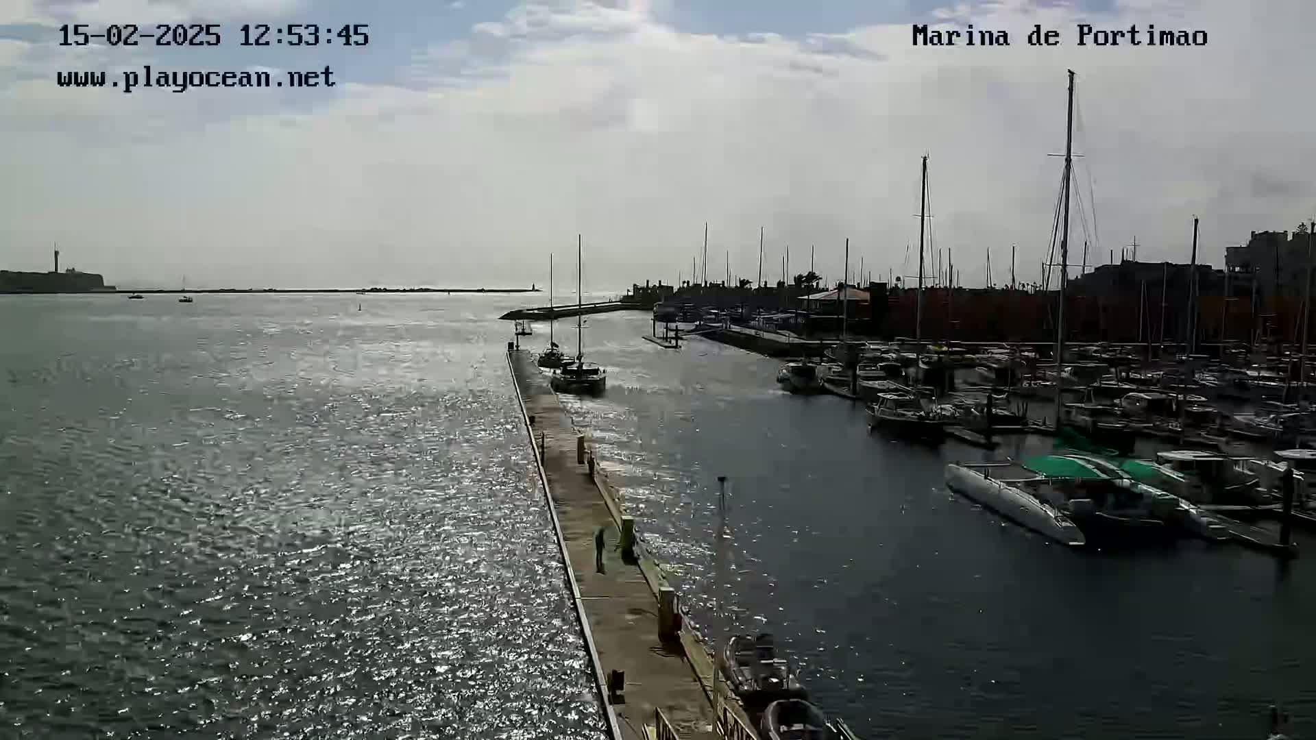 A marina filled with numerous boats is shown on a partly sunny day with a calm, somewhat choppy sea.
