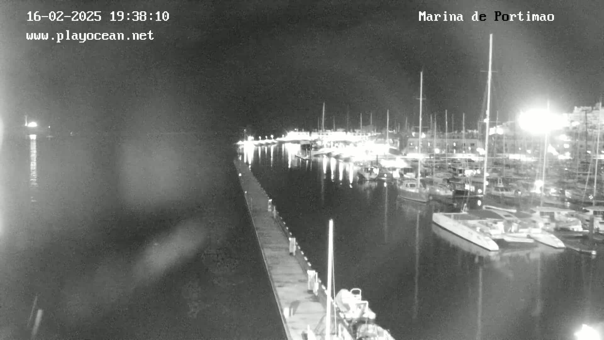 A nighttime, low-light view of a marina filled with docked boats and yachts, seen from a pier.