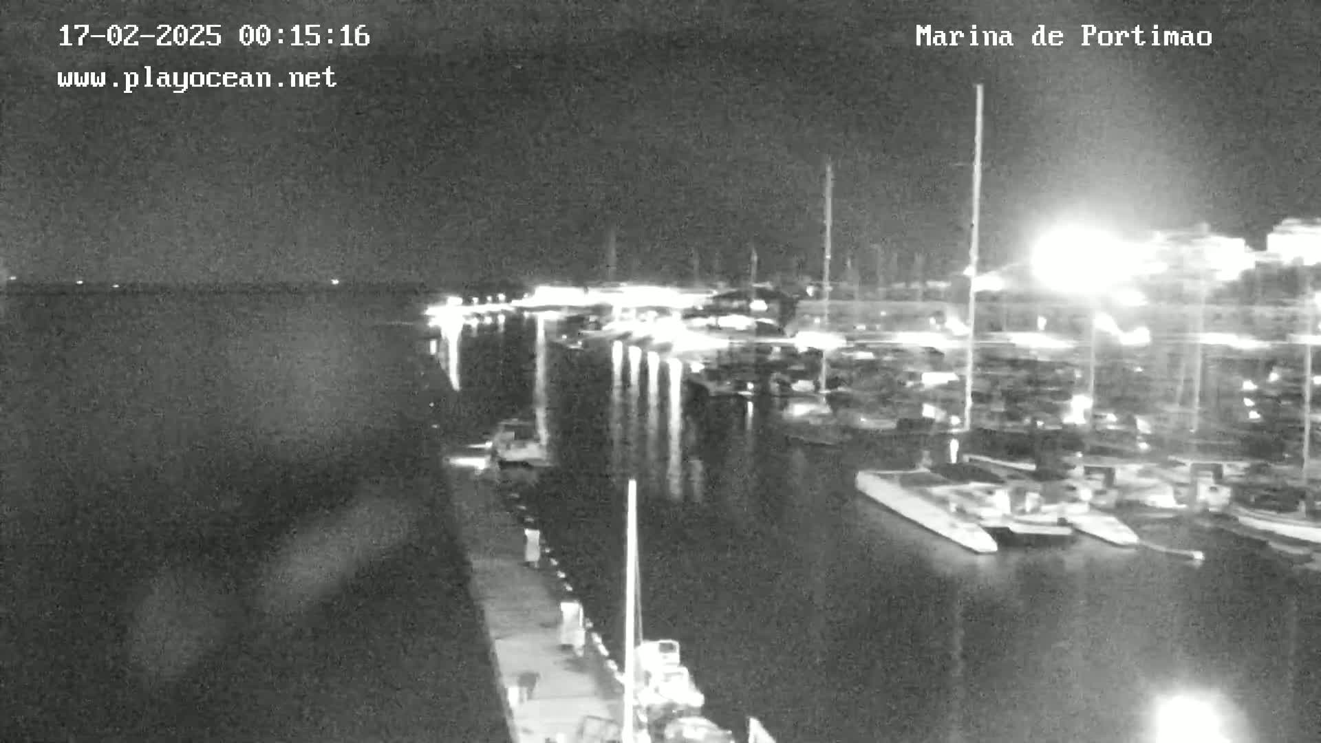 A nighttime, low-light view of a marina with numerous boats docked, illuminated by lights along the docks.