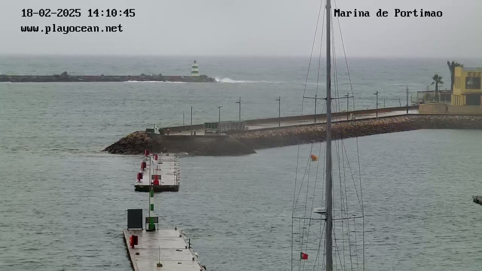 A marina with a lighthouse in the distance, partially obscured by rain and choppy water.