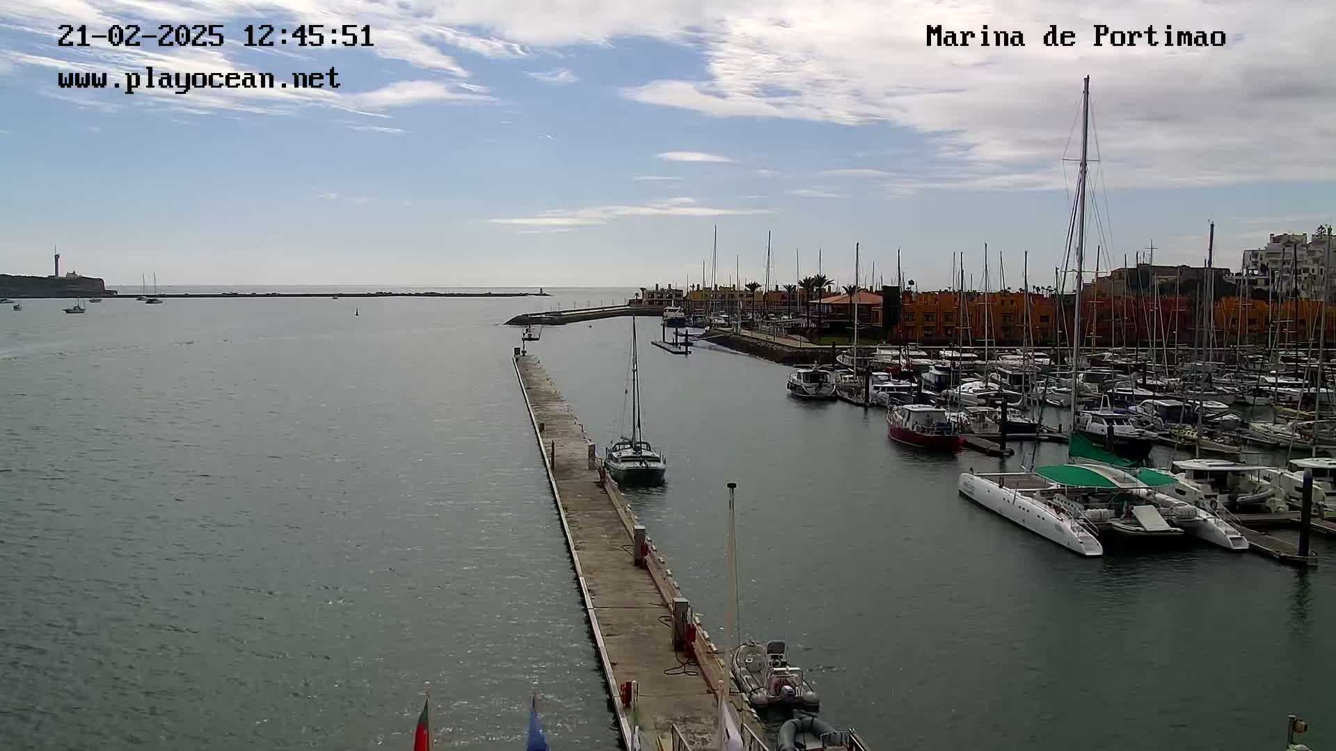 A marina filled with numerous boats and yachts is seen under a partly cloudy sky.