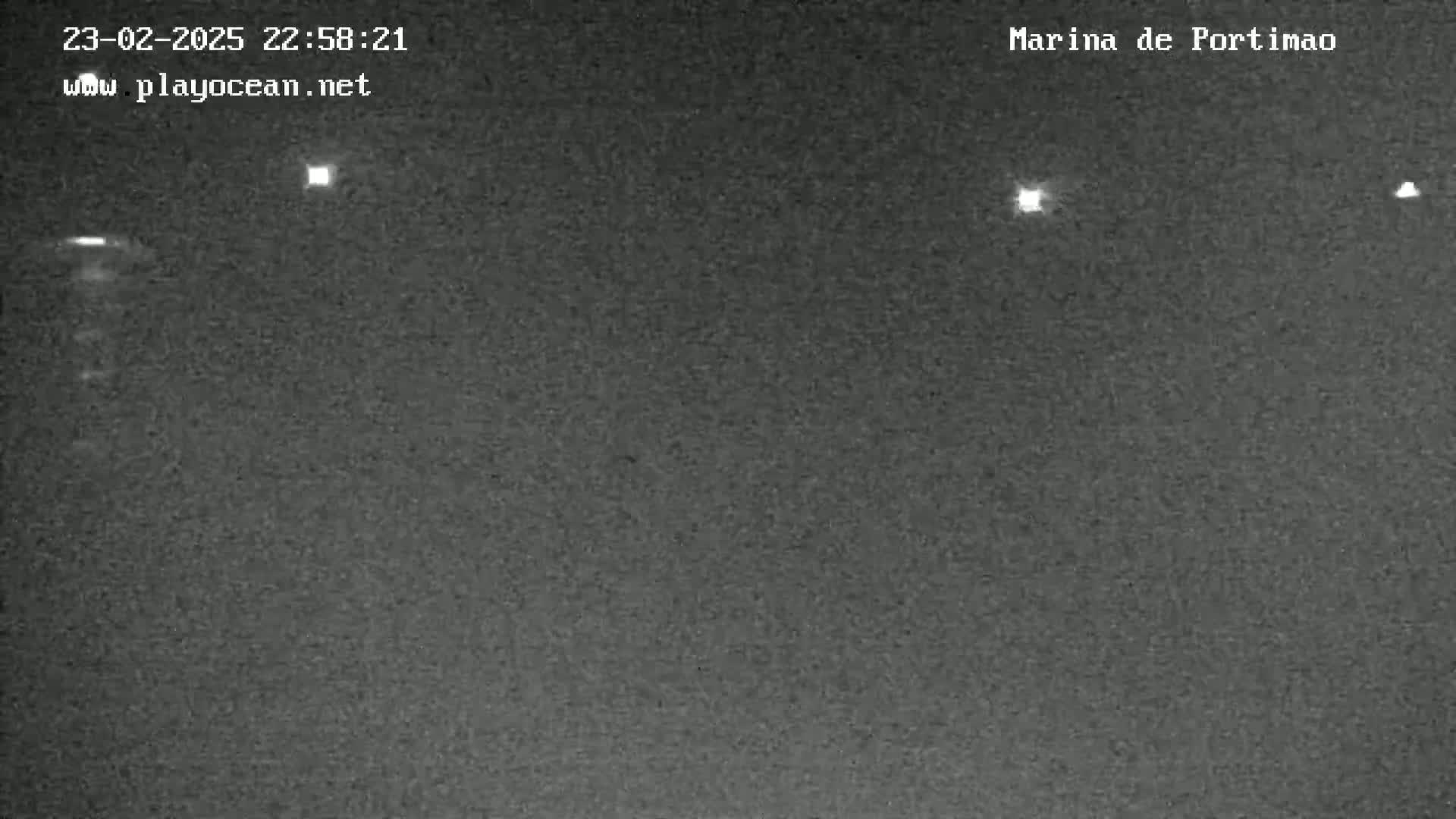 A nighttime, low-light image shows a dark, textured surface with several small, distant lights visible.