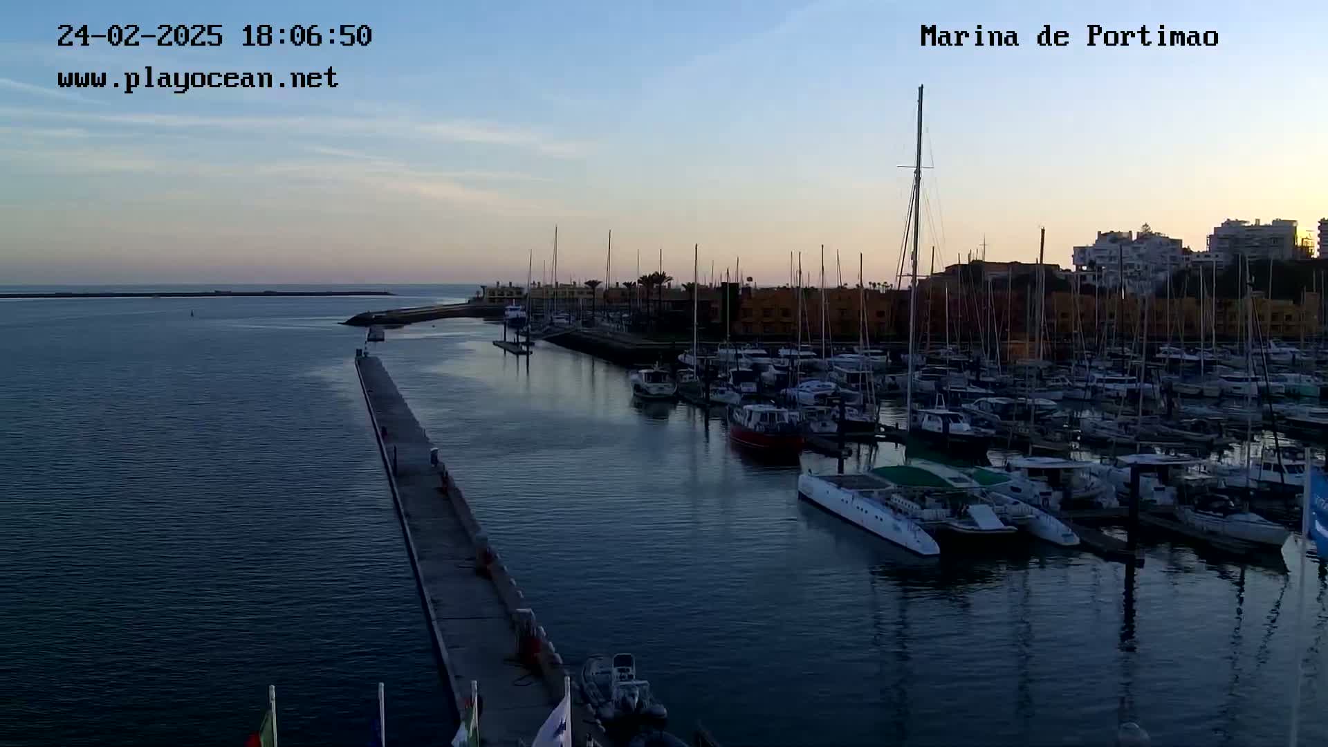 A marina filled with numerous sailboats and motorboats at sunset under a clear sky.