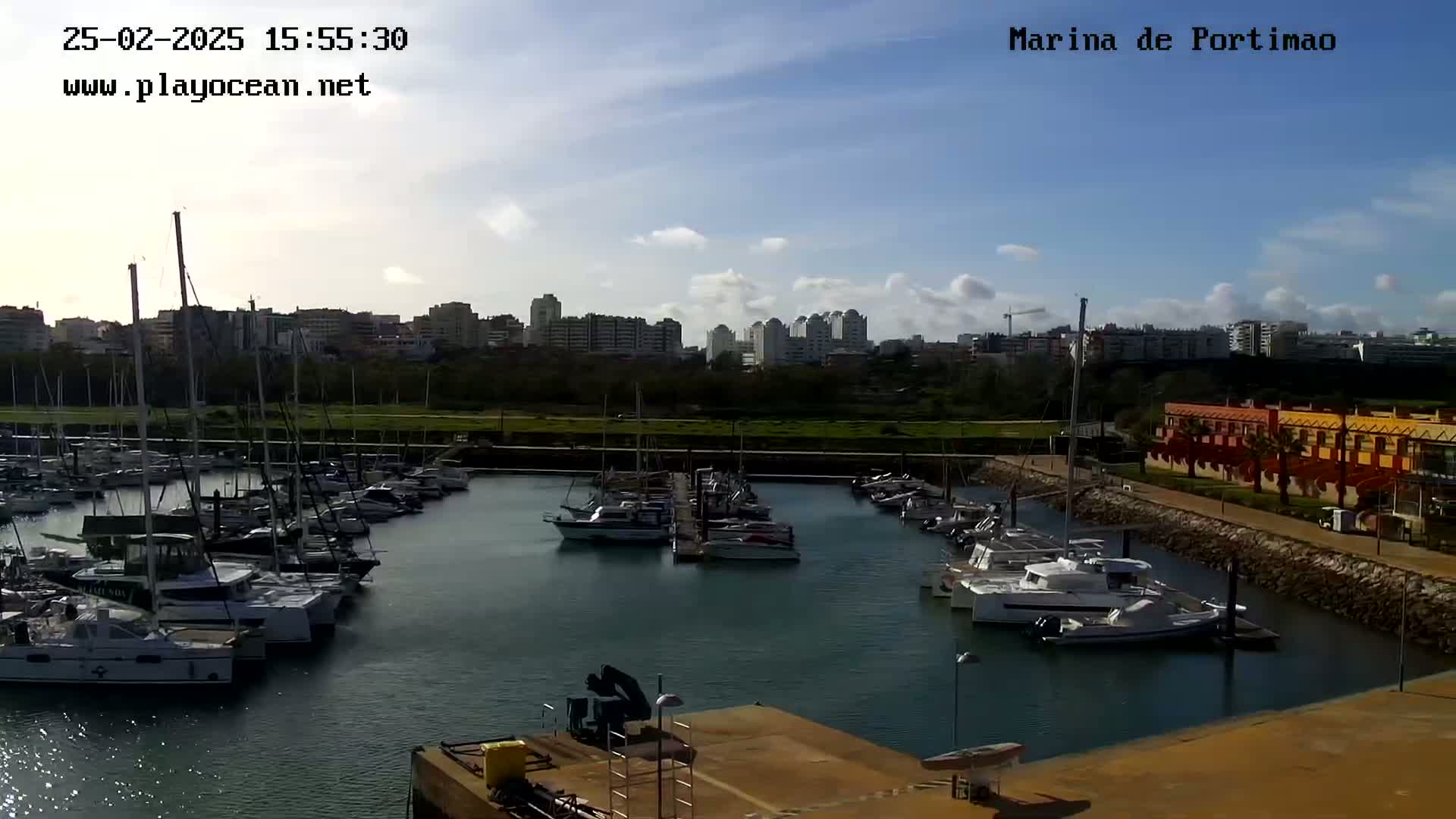 A marina filled with numerous boats is situated in front of a city skyline under a partly cloudy sky.