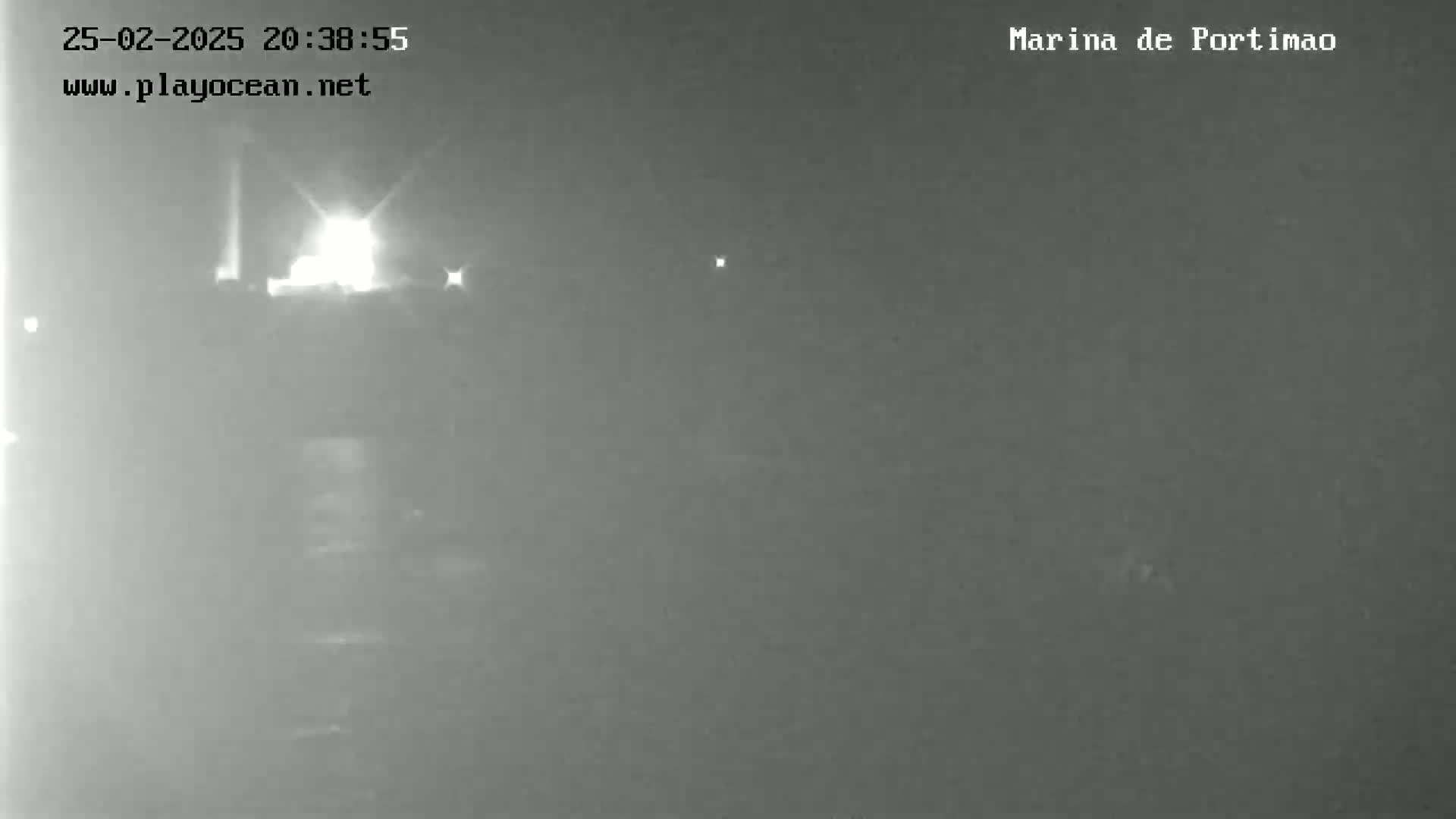 A nighttime, low-light image shows a blurry view of a dimly lit waterfront area, possibly a marina.