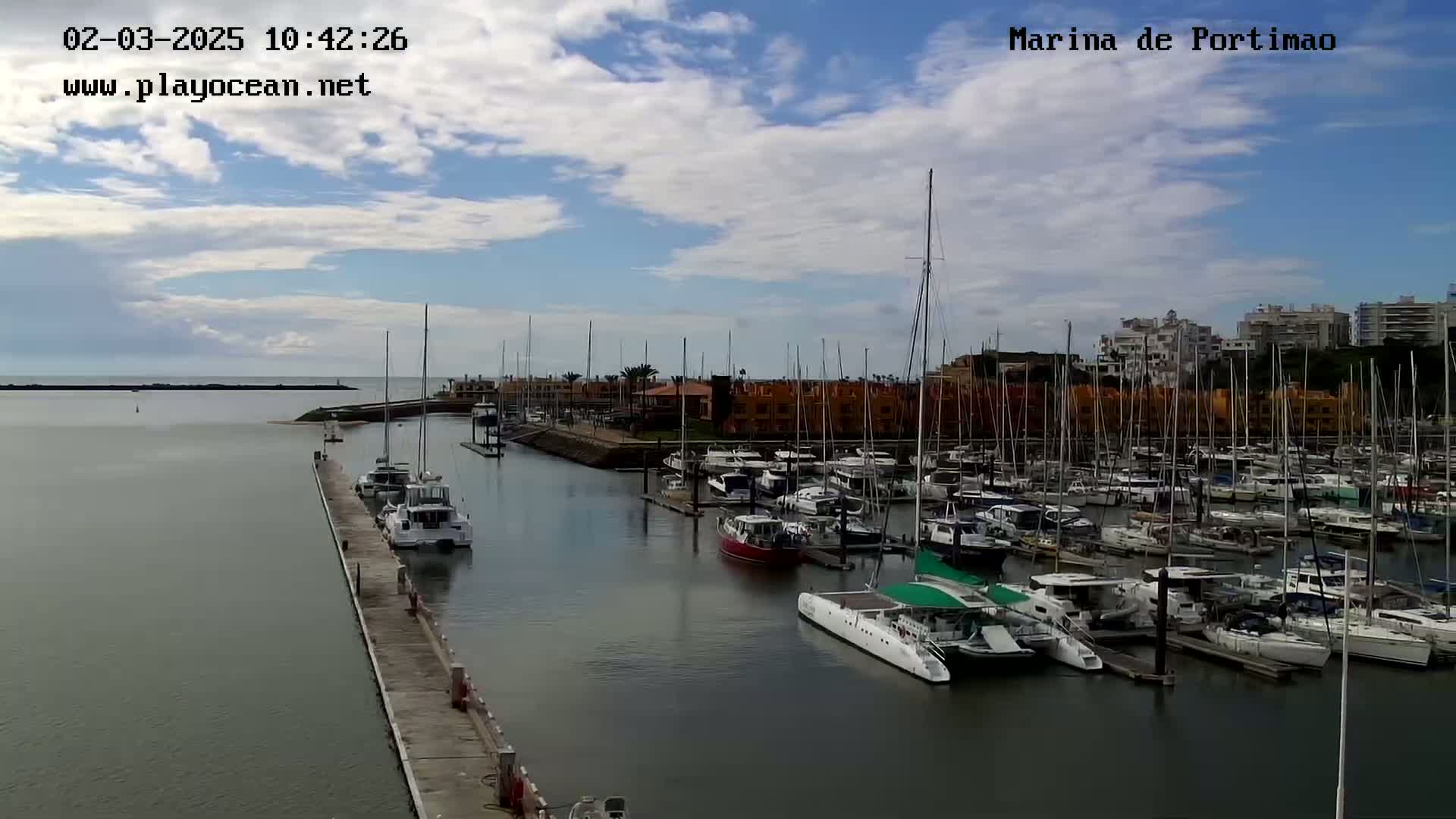 A marina filled with numerous sailboats and motorboats is seen under a partly cloudy sky.