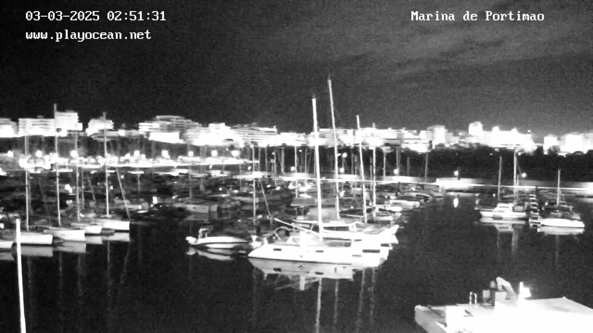 A nighttime view of a marina filled with sailboats and motorboats, under a dark sky.