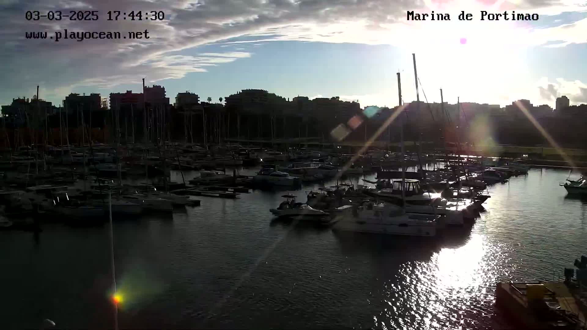 A marina filled with numerous boats is seen at sunset under a partly cloudy sky.
