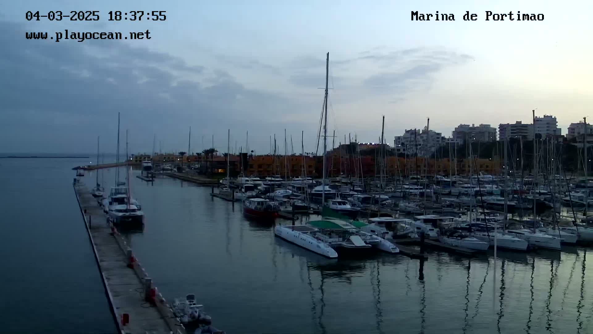 A marina filled with numerous sailboats and motorboats under a cloudy, dusky sky.