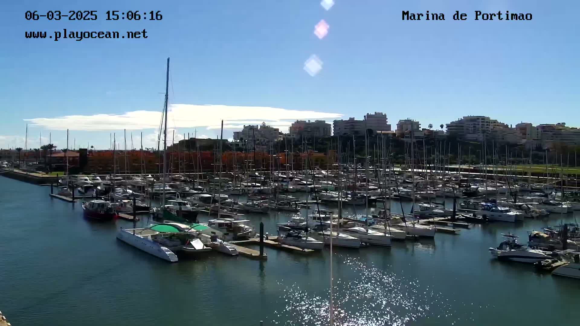 A marina filled with numerous sailboats and motorboats under a mostly sunny sky.