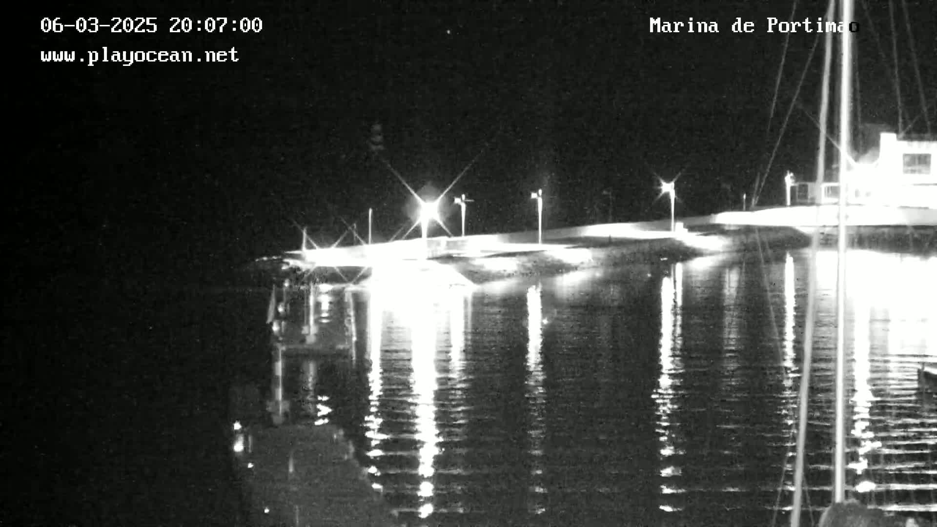A nighttime, brightly lit marina reflects in calm water.