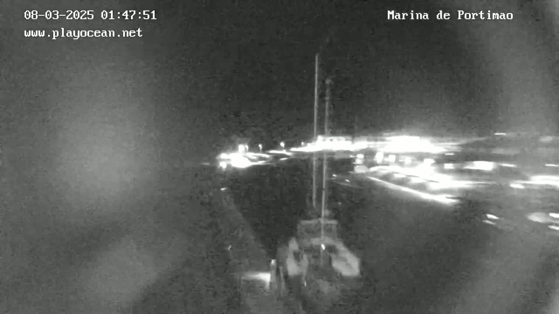 A nighttime, low-light view of a marina shows boats and lights reflecting on the water.