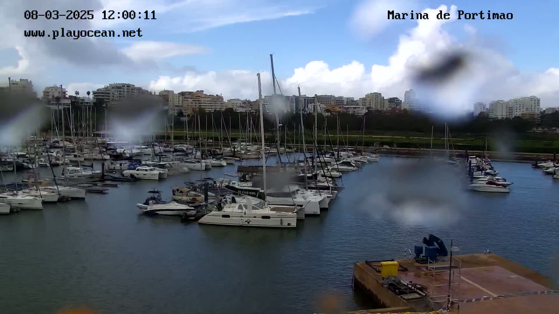 A marina filled with numerous sailboats and motorboats is seen on a cloudy, rainy day.