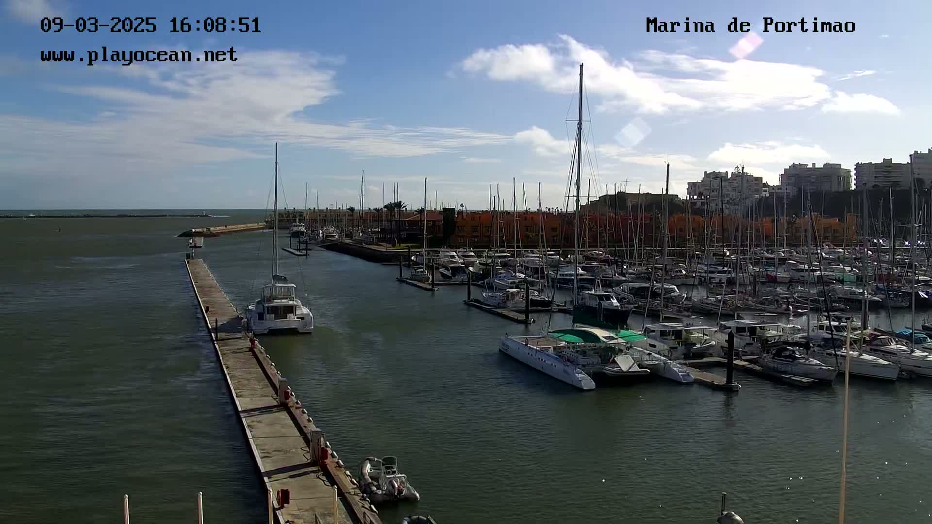 A marina filled with numerous boats and yachts on a partly sunny day with some clouds in the sky.